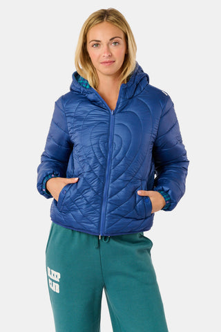 A woman wearing a SOPHISTICA Plaid Hearts Reversible Puffer Jacket, a hooded, zip-front nylon puffer in an emerald green and blue plaid pattern accented by small pink hearts.