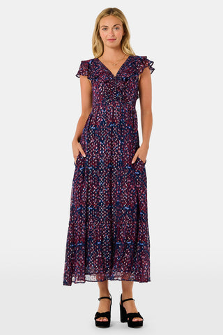 A woman wears a burgundy botanical print SOPHISTICA Rhone Ondine Dress featuring flutter sleeves, a ruffled neckline, and side pockets, paired with black platform heels for a holiday look.