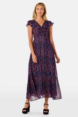 A woman wears a burgundy botanical print SOPHISTICA Rhone Ondine Dress featuring flutter sleeves, a ruffled neckline, and side pockets, paired with black platform heels for a holiday look.