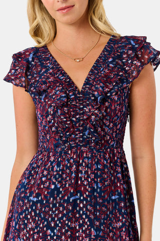 A woman wears a burgundy botanical print SOPHISTICA Rhone Ondine Dress featuring flutter sleeves, a ruffled neckline, and side pockets, paired with black platform heels for a holiday look.