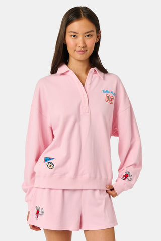 A young woman in the Roller Rabbit Game Day Rugby Sweatshirt and cap smiles while holding a football on a grassy field with trees and buildings in the background.