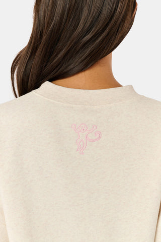A woman wears the ARILCONFEX Sleep Club Andie Sweatshirt, an oatmeal crewneck with SLEEP in pink plaid appliqué across the chest and Club embroidered below it in pink script.