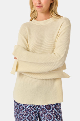 A woman wearing the Roller Rabbit Soleil Sweater, a cream cashmere blend pullover with wide sleeves, paired with patterned blue and white pants, stands against a plain white background.