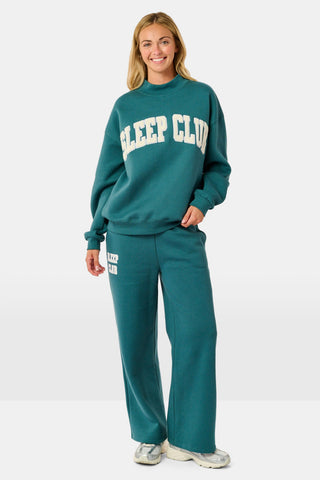 Deep teal wide-leg Sleep Club Mimi Sweatpants in Dream Fleece with an elastic drawstring waist and SLEEP CLUB printed on the right hip.