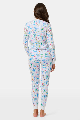 The Kids Game Day Pajamas by Roller Rabbit are a children’s long-sleeve pajama set crafted from soft Pima cotton, featuring a vibrant party-themed print with colorful dinosaurs, bunting, gifts, and party hats on a white background.