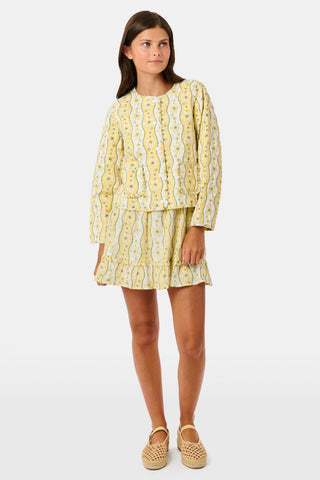 A young girl wearing a Roller Rabbit Kids Lillian Floral Stripe Finn Jacket paired with a matching ruffled skirt and gold ballet flats, standing and smiling against a plain white background—perfect for back-to-school style.