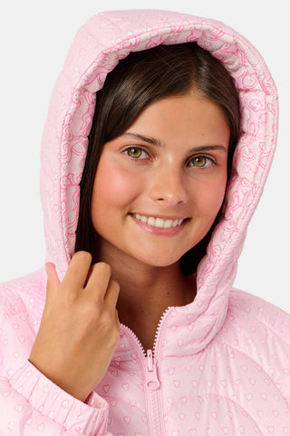 A person wearing a light pink SOPHISTICA Kids Lovely Monkey/Hearts Reversible Puffer Jacket made of durable nylon with repeating heart-shaped quilting and a hood.