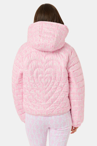 A person wearing a light pink SOPHISTICA Kids Lovely Monkey/Hearts Reversible Puffer Jacket made of durable nylon with repeating heart-shaped quilting and a hood.
