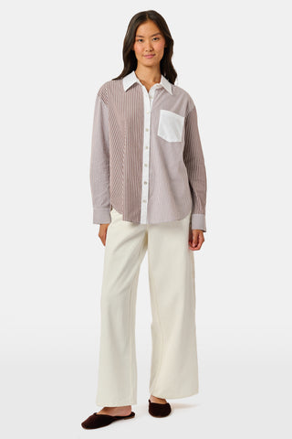 A woman wearing the Roller Rabbit Yarn Dye Stripe Emory Dress—a cotton button-down style with a tie belt and white collar—smiles while looking to the side and pairs the dress with knee-high boots. The background is plain light gray.