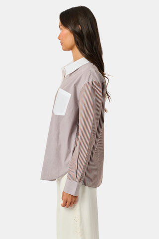 A woman wearing the Roller Rabbit Yarn Dye Stripe Emory Dress—a cotton button-down style with a tie belt and white collar—smiles while looking to the side and pairs the dress with knee-high boots. The background is plain light gray.