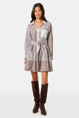 A woman wearing the Roller Rabbit Yarn Dye Stripe Emory Dress—a cotton button-down style with a tie belt and white collar—smiles while looking to the side and pairs the dress with knee-high boots. The background is plain light gray.