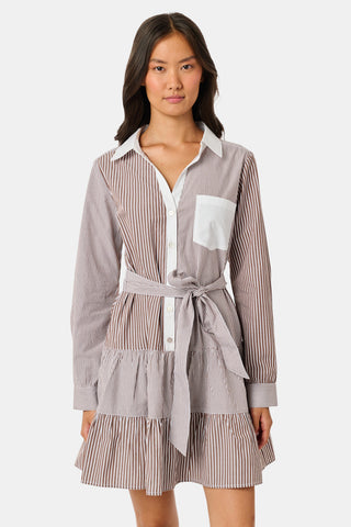 A woman wearing the Roller Rabbit Yarn Dye Stripe Emory Dress—a cotton button-down style with a tie belt and white collar—smiles while looking to the side and pairs the dress with knee-high boots. The background is plain light gray.
