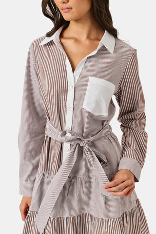 A woman wearing the Roller Rabbit Yarn Dye Stripe Emory Dress—a cotton button-down style with a tie belt and white collar—smiles while looking to the side and pairs the dress with knee-high boots. The background is plain light gray.