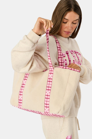 A person holds a beige sherpa Plaid Hearts Sherpa Tote with pink plaid handles and trim, coordinating with a matching pink plaid heart patch on their sweatpants.
