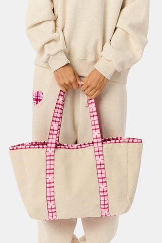 A person holds a beige sherpa Plaid Hearts Sherpa Tote with pink plaid handles and trim, coordinating with a matching pink plaid heart patch on their sweatpants.