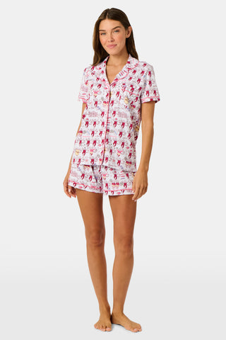 The Roller Rabbit Alpha Phi Monkey Polo Pajamas are a two-piece set crafted from soft Pima Cotton, featuring a white base adorned with playful red cartoon monkey prints and whimsical text. The short-sleeve top includes a front button placket, while the matching shorts feature an elastic waistband, all displayed on a plain background.