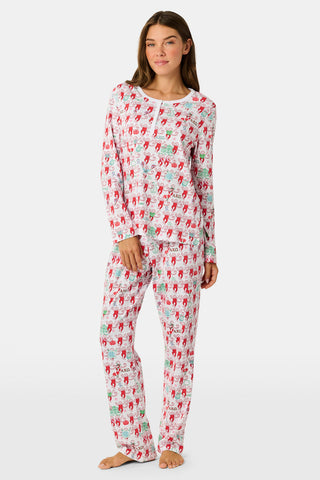 A woman stands outside with her arms crossed, wearing the Roller Rabbit Alpha Chi Omega Monkey Pajamas—a white Henley top and elastic waist pajama set featuring playful red and pink monkey patterns. She holds a matching quilted bag and carries a small heart-shaped blue and white polka dot purse.