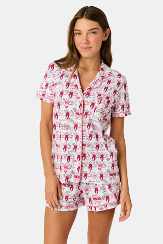 The Roller Rabbit Alpha Phi Monkey Polo Pajamas are a two-piece set crafted from soft Pima Cotton, featuring a white base adorned with playful red cartoon monkey prints and whimsical text. The short-sleeve top includes a front button placket, while the matching shorts feature an elastic waistband, all displayed on a plain background.