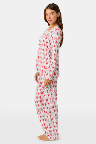 A woman stands outside with her arms crossed, wearing the Roller Rabbit Alpha Chi Omega Monkey Pajamas—a white Henley top and elastic waist pajama set featuring playful red and pink monkey patterns. She holds a matching quilted bag and carries a small heart-shaped blue and white polka dot purse.