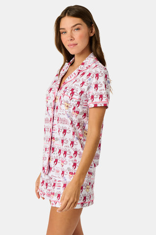 The Roller Rabbit Alpha Phi Monkey Polo Pajamas are a two-piece set crafted from soft Pima Cotton, featuring a white base adorned with playful red cartoon monkey prints and whimsical text. The short-sleeve top includes a front button placket, while the matching shorts feature an elastic waistband, all displayed on a plain background.