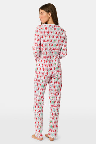 A woman stands outside with her arms crossed, wearing the Roller Rabbit Alpha Chi Omega Monkey Pajamas—a white Henley top and elastic waist pajama set featuring playful red and pink monkey patterns. She holds a matching quilted bag and carries a small heart-shaped blue and white polka dot purse.