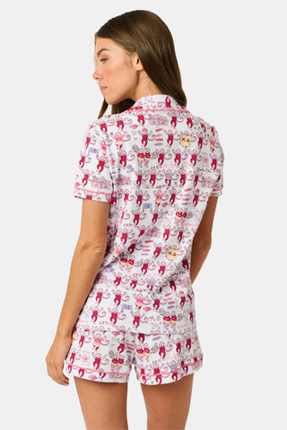 The Roller Rabbit Alpha Phi Monkey Polo Pajamas are a two-piece set crafted from soft Pima Cotton, featuring a white base adorned with playful red cartoon monkey prints and whimsical text. The short-sleeve top includes a front button placket, while the matching shorts feature an elastic waistband, all displayed on a plain background.