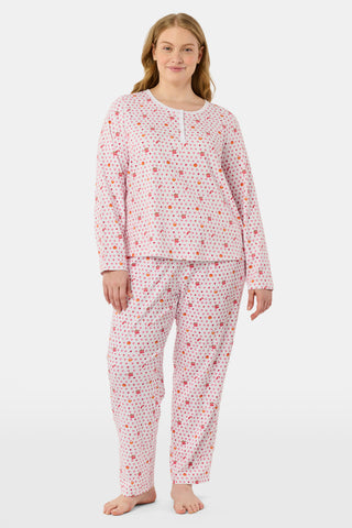 A person stands facing forward, barefoot against a plain white background, wearing Roller Rabbit’s Autumn Hearts Pajamas—women’s long-sleeve and long-pant pajamas crafted from soft Pima cotton in a pink and white polka-dot print.