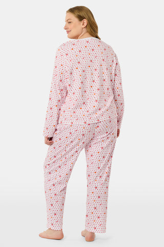 A person stands facing forward, barefoot against a plain white background, wearing Roller Rabbit’s Autumn Hearts Pajamas—women’s long-sleeve and long-pant pajamas crafted from soft Pima cotton in a pink and white polka-dot print.