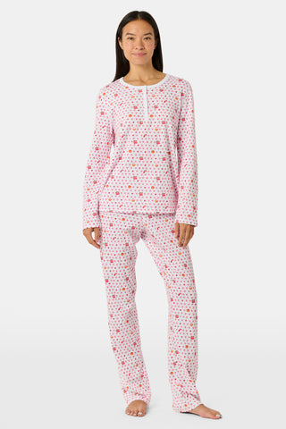 A person stands facing forward, barefoot against a plain white background, wearing Roller Rabbit’s Autumn Hearts Pajamas—women’s long-sleeve and long-pant pajamas crafted from soft Pima cotton in a pink and white polka-dot print.