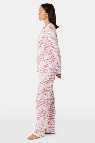 A person stands facing forward, barefoot against a plain white background, wearing Roller Rabbit’s Autumn Hearts Pajamas—women’s long-sleeve and long-pant pajamas crafted from soft Pima cotton in a pink and white polka-dot print.