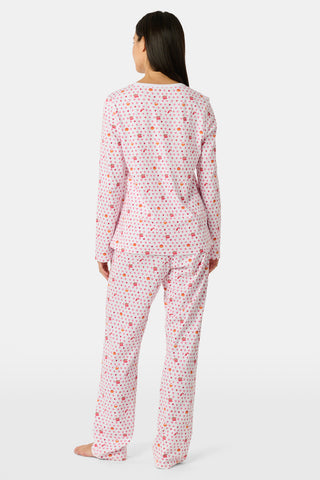 A person stands facing forward, barefoot against a plain white background, wearing Roller Rabbit’s Autumn Hearts Pajamas—women’s long-sleeve and long-pant pajamas crafted from soft Pima cotton in a pink and white polka-dot print.