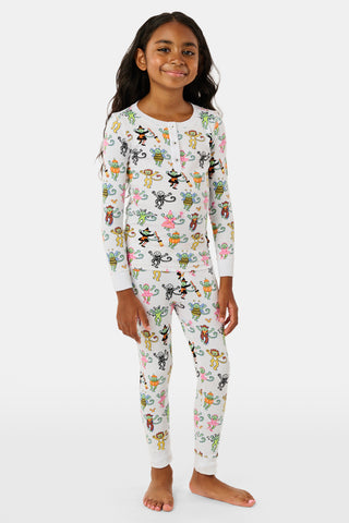 A smiling child in Roller Rabbit’s Kids Boo Crew Pajamas, crafted from soft Pima cotton, sits with arms raised on outdoor steps among women in coordinating patterned pajamas, all sharing a cheerful and relaxed moment together.
