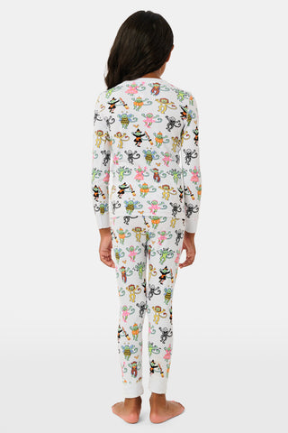 A smiling child in Roller Rabbit’s Kids Boo Crew Pajamas, crafted from soft Pima cotton, sits with arms raised on outdoor steps among women in coordinating patterned pajamas, all sharing a cheerful and relaxed moment together.