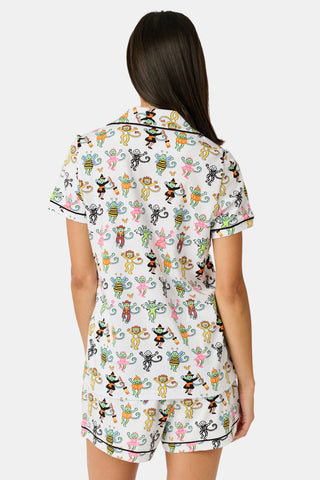 A smiling child in Roller Rabbit’s Kids Boo Crew Pajamas, crafted from soft Pima cotton, sits with arms raised on outdoor steps among women in coordinating patterned pajamas, all sharing a cheerful and relaxed moment together.