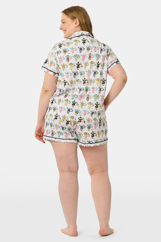 A smiling child in Roller Rabbit’s Kids Boo Crew Pajamas, crafted from soft Pima cotton, sits with arms raised on outdoor steps among women in coordinating patterned pajamas, all sharing a cheerful and relaxed moment together.