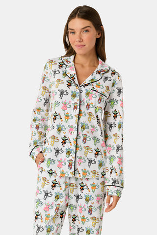 A smiling child in Roller Rabbit’s Kids Boo Crew Pajamas, crafted from soft Pima cotton, sits with arms raised on outdoor steps among women in coordinating patterned pajamas, all sharing a cheerful and relaxed moment together.