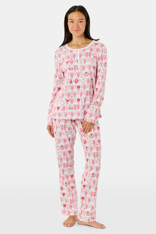 The Roller Rabbit Chi Omega Monkey Pajamas are a long-sleeve Henley top pajama set with matching pants, featuring a white background decorated with red, pink, and gray hearts, XOXO motifs, and playful accents. The pants are designed with a comfortable mid-rise elastic waist.