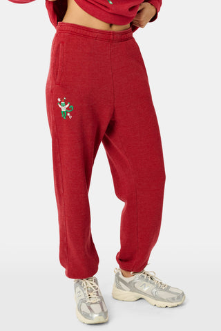 Holly berry red US BLANKS Deck The Halls Bea Sweatpants featuring a small embroidered graphic of a green character wearing a holiday sweater on the right hip.