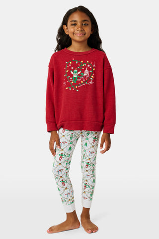 A child wears a Kids Deck The Halls Andie Sweatshirt featuring a heart made of festive lights, a cartoon monkey, and a Christmas tree graphic, paired with patterned leggings showing elves and snowmen.
