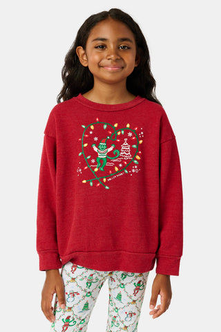 A child wears a Kids Deck The Halls Andie Sweatshirt featuring a heart made of festive lights, a cartoon monkey, and a Christmas tree graphic, paired with patterned leggings showing elves and snowmen.