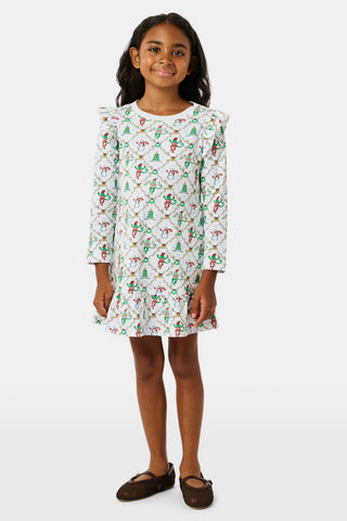 A young girl wears a Kids Deck The Halls Isa Dress, a long-sleeved Pima Cotton holiday dress featuring a white background with a festive monkey print of snowmen and Christmas trees.