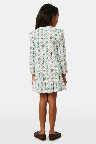 A young girl wears a Kids Deck The Halls Isa Dress, a long-sleeved Pima Cotton holiday dress featuring a white background with a festive monkey print of snowmen and Christmas trees.