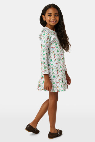 A young girl wears a Kids Deck The Halls Isa Dress, a long-sleeved Pima Cotton holiday dress featuring a white background with a festive monkey print of snowmen and Christmas trees.
