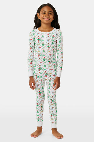 A child wearing SERFLEX Kids Deck The Halls Pajamas, featuring a repeating holiday pattern of snowmen, Christmas trees, and elves connected by garland on long-sleeved Pima cotton.