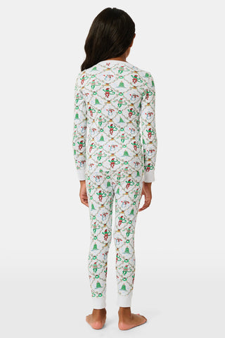 A child wearing SERFLEX Kids Deck The Halls Pajamas, featuring a repeating holiday pattern of snowmen, Christmas trees, and elves connected by garland on long-sleeved Pima cotton.