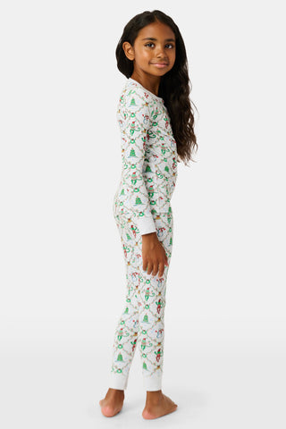 A child wearing SERFLEX Kids Deck The Halls Pajamas, featuring a repeating holiday pattern of snowmen, Christmas trees, and elves connected by garland on long-sleeved Pima cotton.