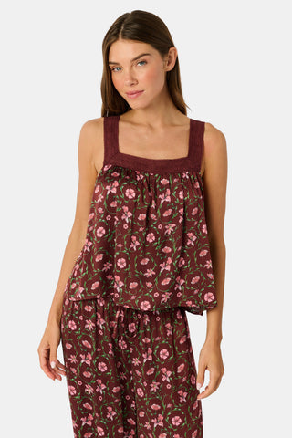 A woman wears a burgundy Greta Floral Ditsy Rowan Set camisole and wide-leg trousers, standing in front of a rustic wooden fence decorated with Christmas stockings.