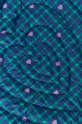A woman wearing a SOPHISTICA Plaid Hearts Reversible Puffer Jacket, a hooded, zip-front nylon puffer in an emerald green and blue plaid pattern accented by small pink hearts.