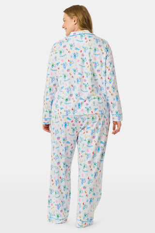 Roller Rabbit’s Game Day Long Sleeve Polo Pajamas feature a white button-up shirt and matching pants adorned with colorful, playful animal prints, festive bunting, and other cheerful designs.