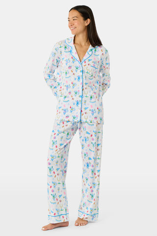Roller Rabbit’s Game Day Long Sleeve Polo Pajamas feature a white button-up shirt and matching pants adorned with colorful, playful animal prints, festive bunting, and other cheerful designs.